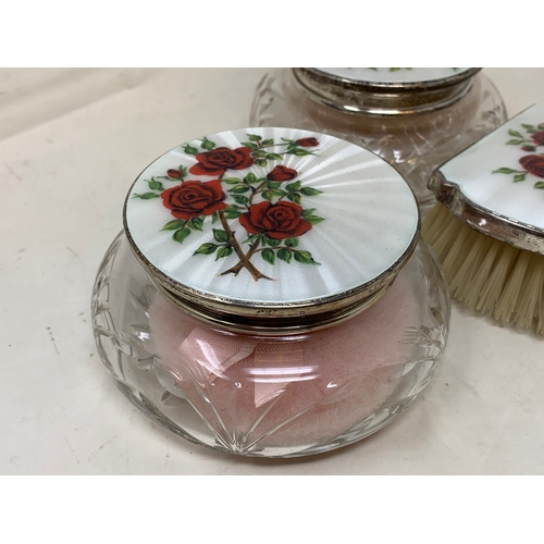 53 - A silver and enamel seven piece dressing table set, decorated roses, Birmingham 1959