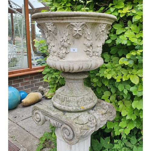 16 - A pair of reconstituted stone garden urns, decorated face masks and foliage, on Ionic type columns, ...