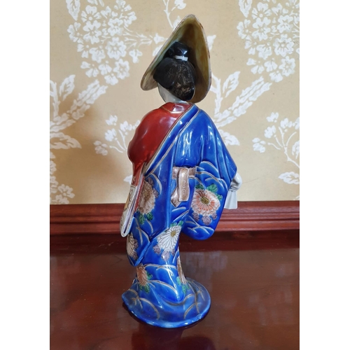 306 - A Japanese porcelain figure of a geisha girl, wearing a hat, 27 cm high