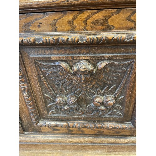 773 - An oak buffet, the top having two drawers, above an open section, above two cupboard doors, carved w... 