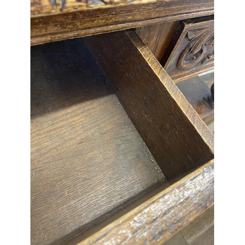 773 - An oak buffet, the top having two drawers, above an open section, above two cupboard doors, carved w... 