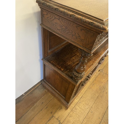 773 - An oak buffet, the top having two drawers, above an open section, above two cupboard doors, carved w... 