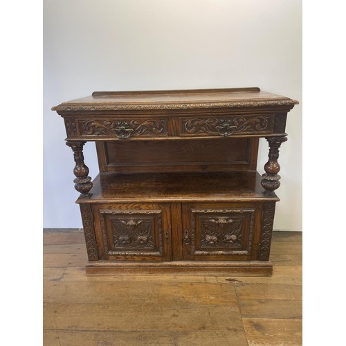 508 - An oak buffet, the top having two drawers, above an open section, above two cupboard doors, carved w... 