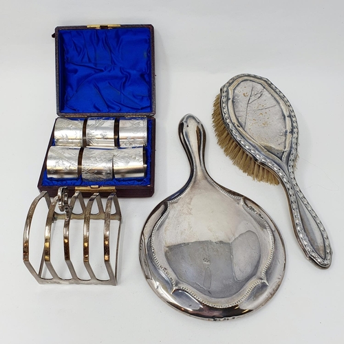 627 - A silver toast rack, set of aesthetic style napkin rings, a silver backed mirror and brush, various ... 