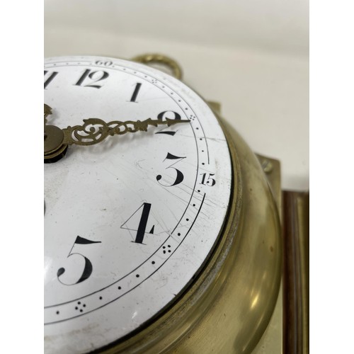 656 - A wall clock, the 11 cm diameter enamel dial with Arabic numerals, in a brass case mounted on an oak... 