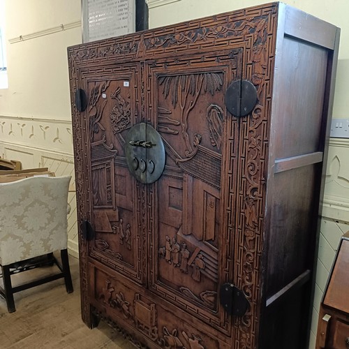 863 - A Chinese two door wardrobe, carved a town scene with figures, 170 cm high x 131 cm wide