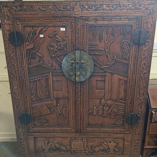 863 - A Chinese two door wardrobe, carved a town scene with figures, 170 cm high x 131 cm wide