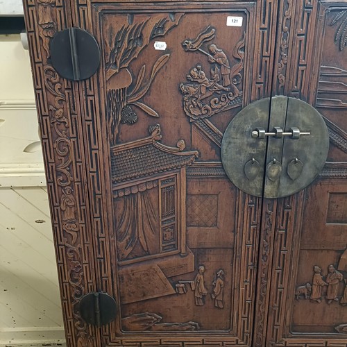 863 - A Chinese two door wardrobe, carved a town scene with figures, 170 cm high x 131 cm wide