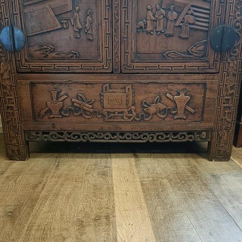 863 - A Chinese two door wardrobe, carved a town scene with figures, 170 cm high x 131 cm wide