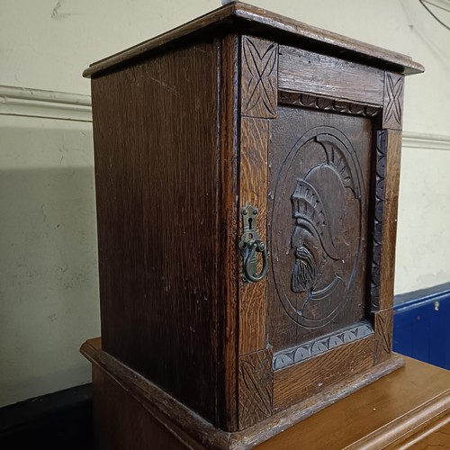 930 - An oak cabinet, the door carved a bust portrait, to reveal three drawers, 33 cm wide