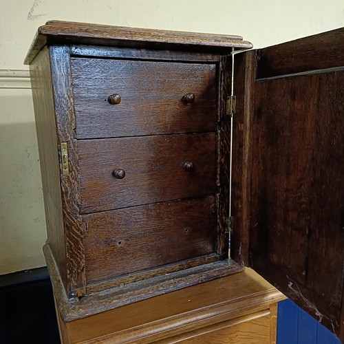 930 - An oak cabinet, the door carved a bust portrait, to reveal three drawers, 33 cm wide