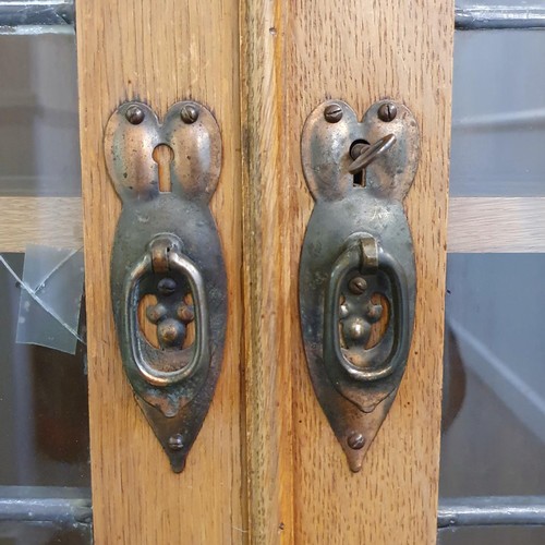 145 - An Arts & Crafts 'Grosvenor' oak bookcase, with two leaded glazed doors, decorated heart shaped moti... 