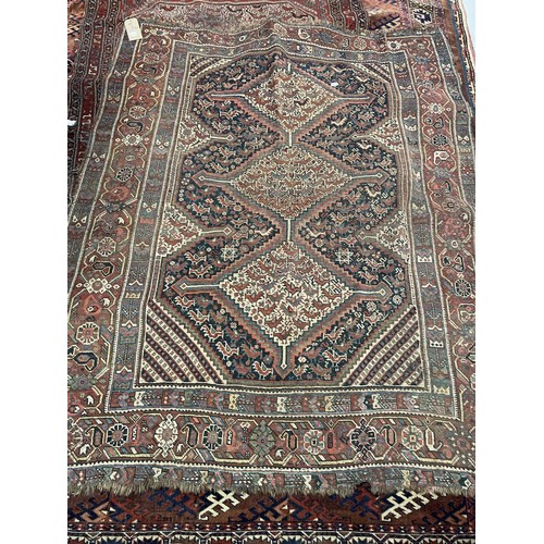 945 - A Persian red ground carpet multiple borders, the centre with three lozenge shaped stepped medallion... 