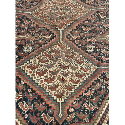 945 - A Persian red ground carpet multiple borders, the centre with three lozenge shaped stepped medallion... 