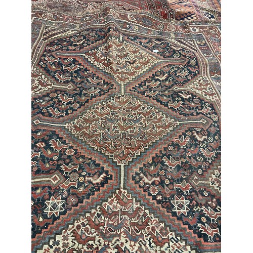 945 - A Persian red ground carpet multiple borders, the centre with three lozenge shaped stepped medallion... 