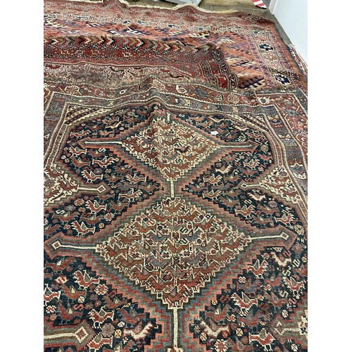 945 - A Persian red ground carpet multiple borders, the centre with three lozenge shaped stepped medallion... 