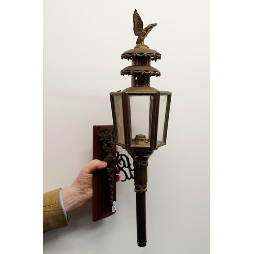 137 - An early 20th century brass oil carriage lamp, with an eagle finial, 59 cm high, mounted on a wooden... 