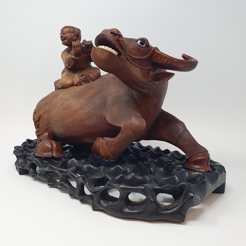 342 - A Chinese carving of a water buffalo, with a seated figure, on a hardwood stand, 40 cm high