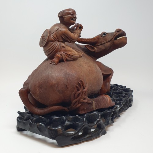 342 - A Chinese carving of a water buffalo, with a seated figure, on a hardwood stand, 40 cm high