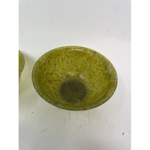 377 - A pair of Chinese carved green stone bowls, 10 cm diameter, on wooden stands (2)