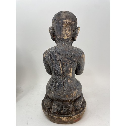 386 - An oriental figure of a praying man, 26 cm high, another similar, 27 cm high, and a carved stone fig... 