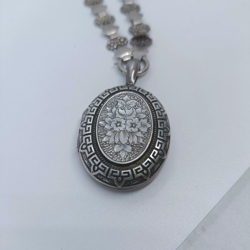 114 - A silver oval locket, on a fancy chain