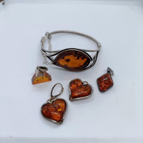 146 - An amber and silver coloured metal bangle, and four similar pendants