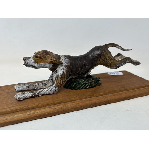 706 - A cold painted bronze clip, in the form of a hound, on a wooden base, 27 cm wide