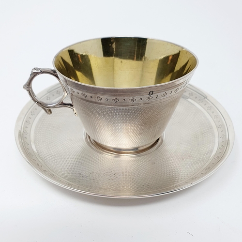 147 - A French silver coloured metal cup and saucer, monogrammed, and with engraved decoration, the saucer... 