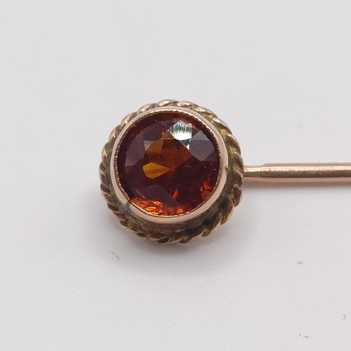 596 - An early 20th century yellow coloured metal and orange stone stick pin  Provenance:  From a single o... 