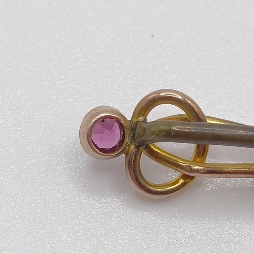 595 - A late 19th/early 20th century yellow coloured metal and amethyst stick pin, in the form of a knot P... 