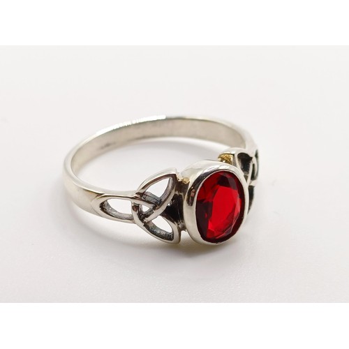 718 - A silver celtic style ring, set with an oval red CZ