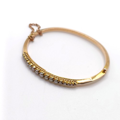 702 - A yellow metal and seed pearl bangle