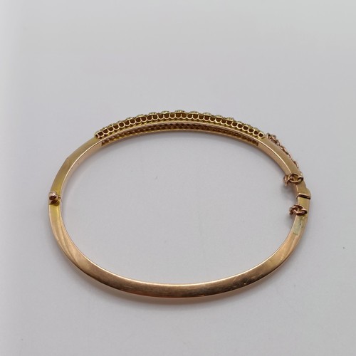 702 - A yellow metal and seed pearl bangle