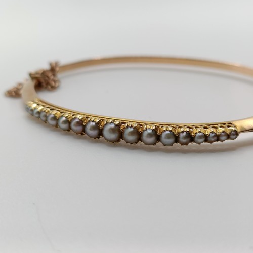 702 - A yellow metal and seed pearl bangle