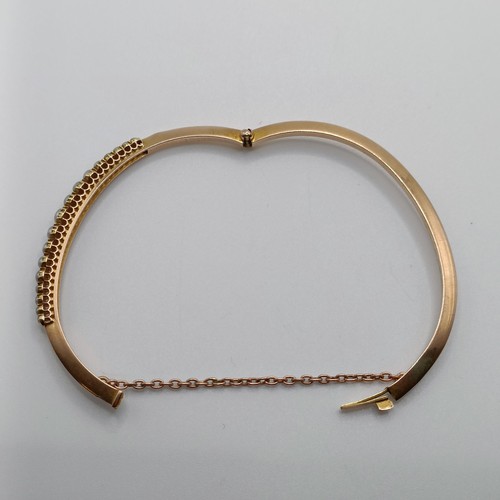 702 - A yellow metal and seed pearl bangle