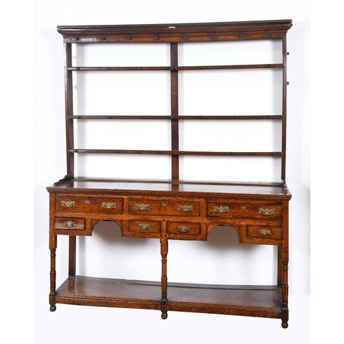 1658 - An 18th century oak dresser, with a three tier plate rack, on a base with seven drawers, above an un... 