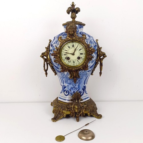 513 - A mantel clock, the enamel dial with Roman numerals, in a Delft case with gilt metal mounts, 47 cm h... 