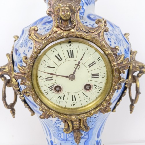 513 - A mantel clock, the enamel dial with Roman numerals, in a Delft case with gilt metal mounts, 47 cm h... 