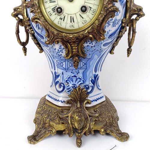 513 - A mantel clock, the enamel dial with Roman numerals, in a Delft case with gilt metal mounts, 47 cm h... 