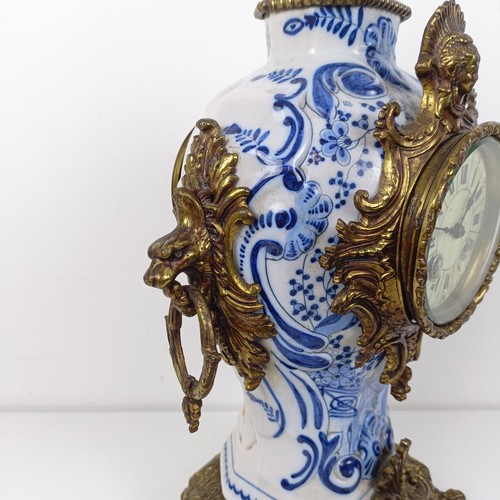 513 - A mantel clock, the enamel dial with Roman numerals, in a Delft case with gilt metal mounts, 47 cm h... 