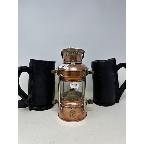 762 - Two modern leather mugs, a brass and copper lantern, two alarm clocks, and a brass syringe (6)