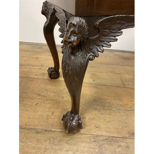 1575 - A walnut stool, with legs carved angel face masks, on claw and ball feet, 110 cm wide