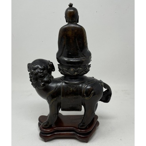 1545 - A Chinese bronze group, of a Buddha seated atop a Shi Shi dog, 26 cm high, on a hardwood stand