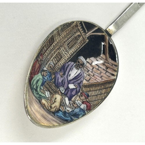 103 - A silver coloured metal and enamel teaspoon, decorated in the Egyptian manner, the finial inlaid wit... 