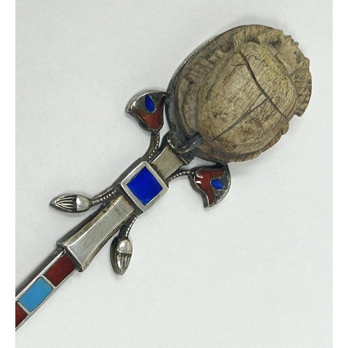 103 - A silver coloured metal and enamel teaspoon, decorated in the Egyptian manner, the finial inlaid wit... 