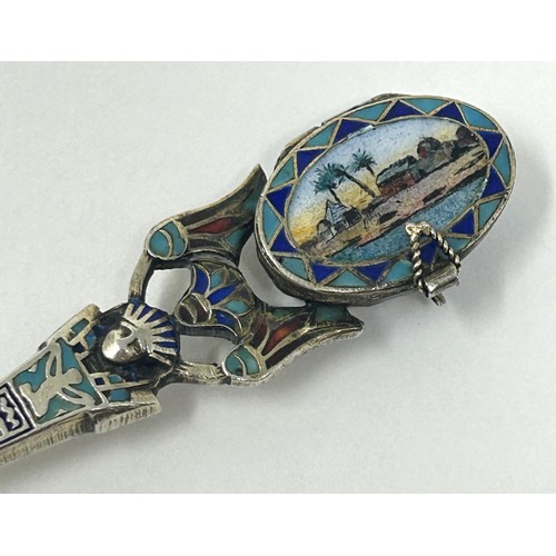 102 - A silver coloured metal and enamel spoon, decorated ancient Egyptian symbols, the finial containing ... 