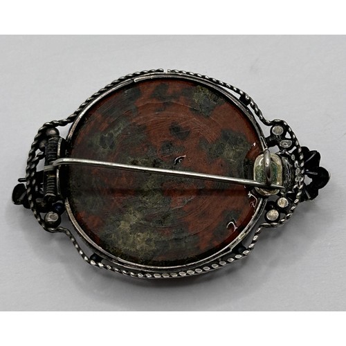 404 - An Arts and Crafts silver coloured metal and red stone brooch and a silver coloured metal and green ... 