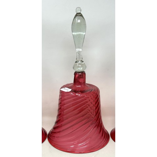 915 - A cranberry and clear glass bell, 34 cm high, and two others, all lacking ringers (3)