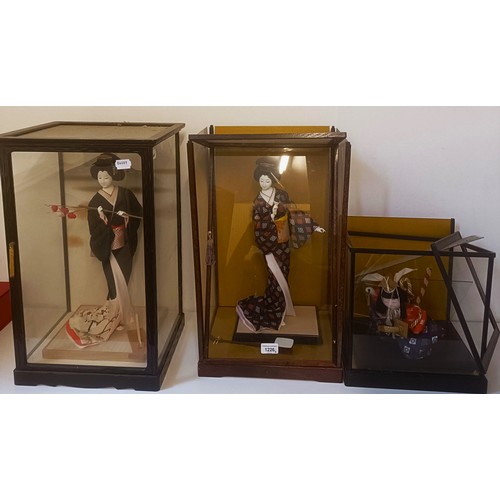 1226 - A Japanese doll, in traditional dress, in a glazed case, 54 cm high, and two others similar (3)